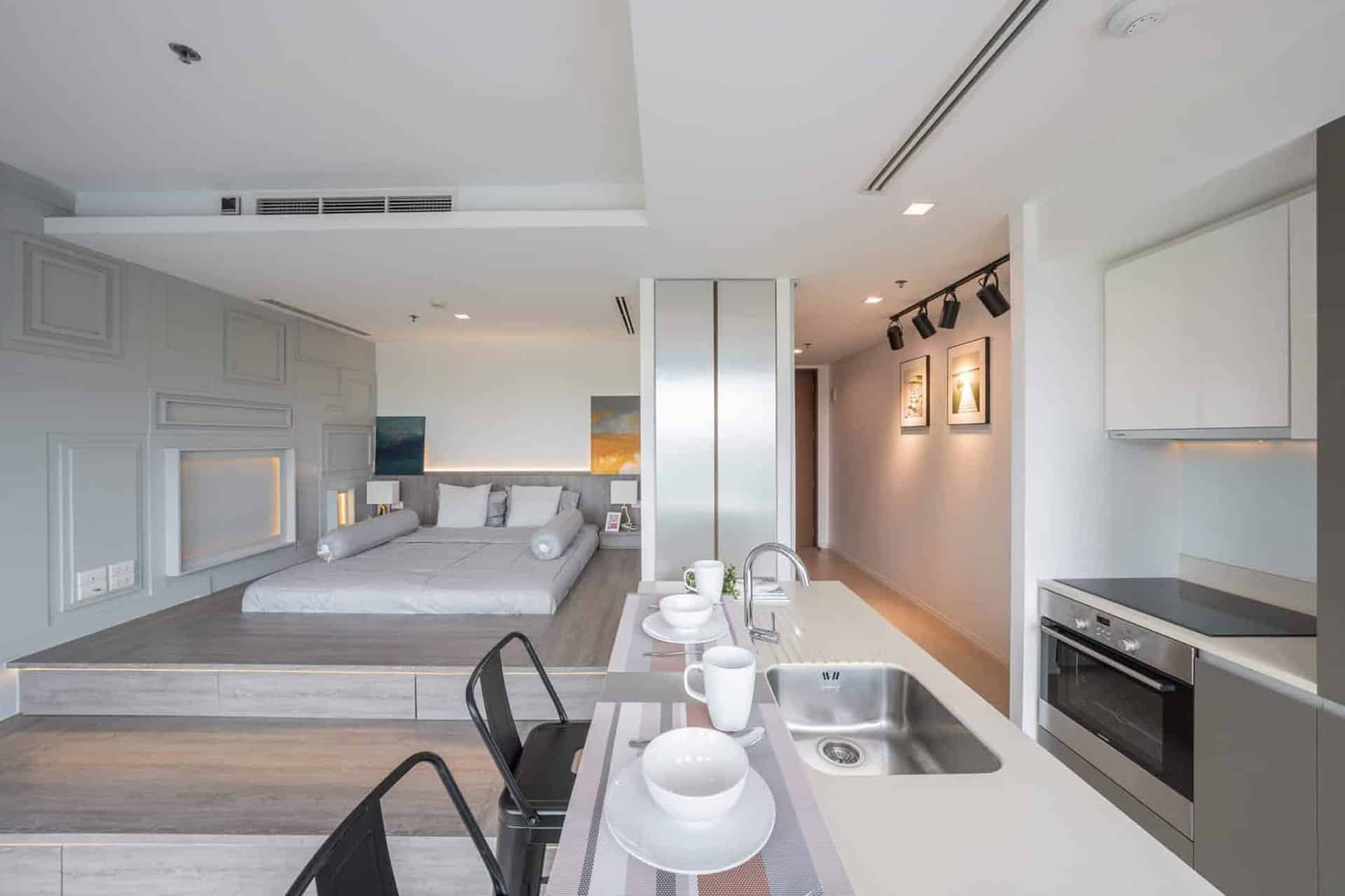 Modern studio apartment in Bangkok featuring open-plan layout with built-in kitchen, dining counter, and elevated bedroom area.