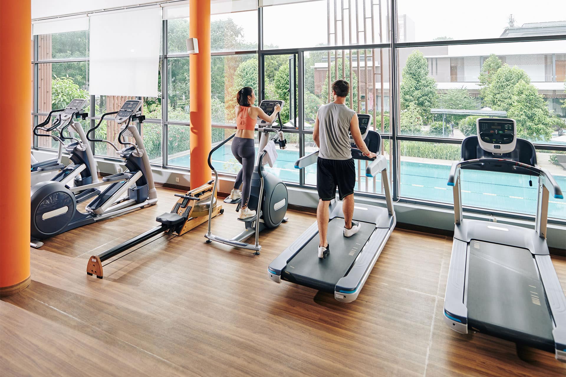 Luxury apartment gym in Bangkok featuring state-of-the-art fitness equipment and poolside view, promoting active urban lifestyle.