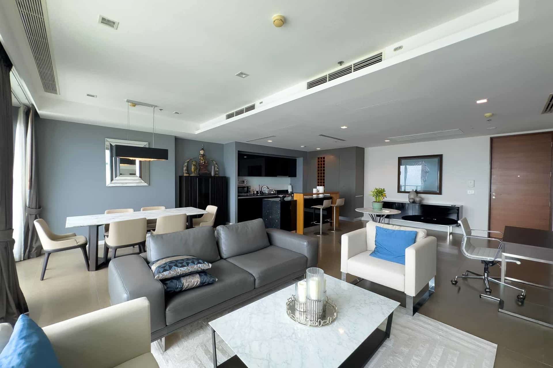 Spacious modern condominium living room in Bangkok with leather sofa, dining area, open kitchen, and contemporary décor.