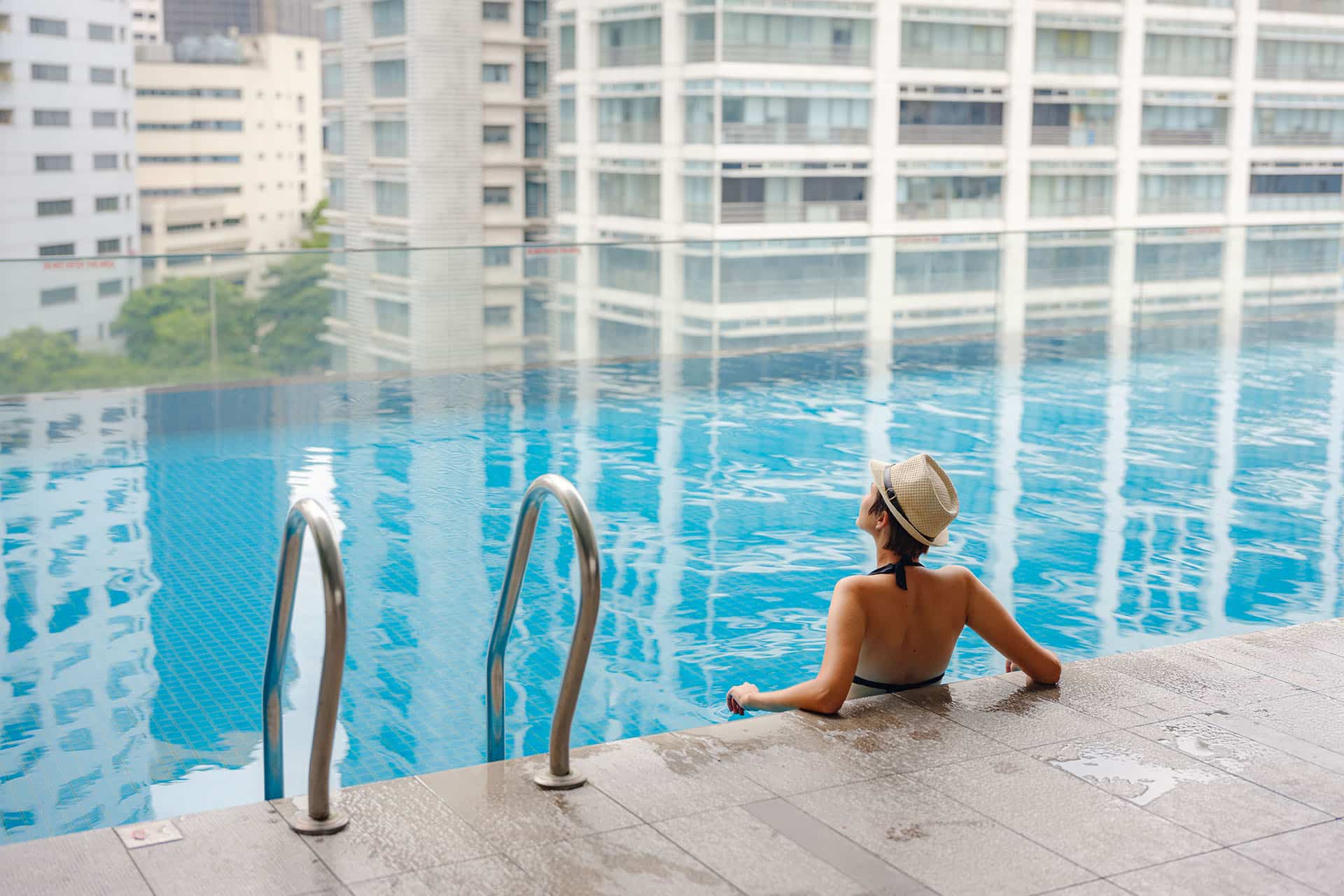 Guest enjoying infinity pool with city views at a luxury Bangkok hotel, highlighting urban relaxation and leisure amenities.